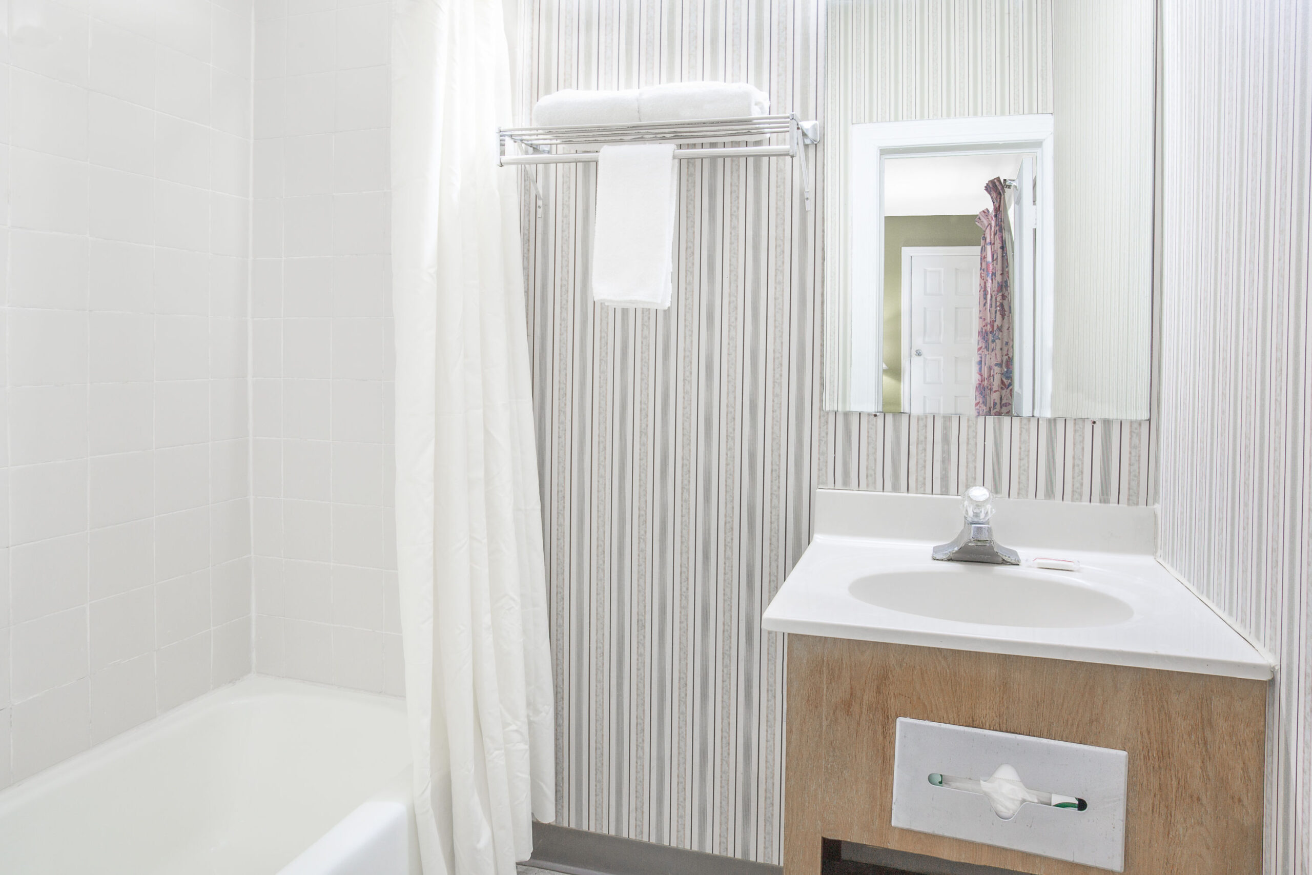 Compact bathroom with bathtub, sink, and striped wallpaper.