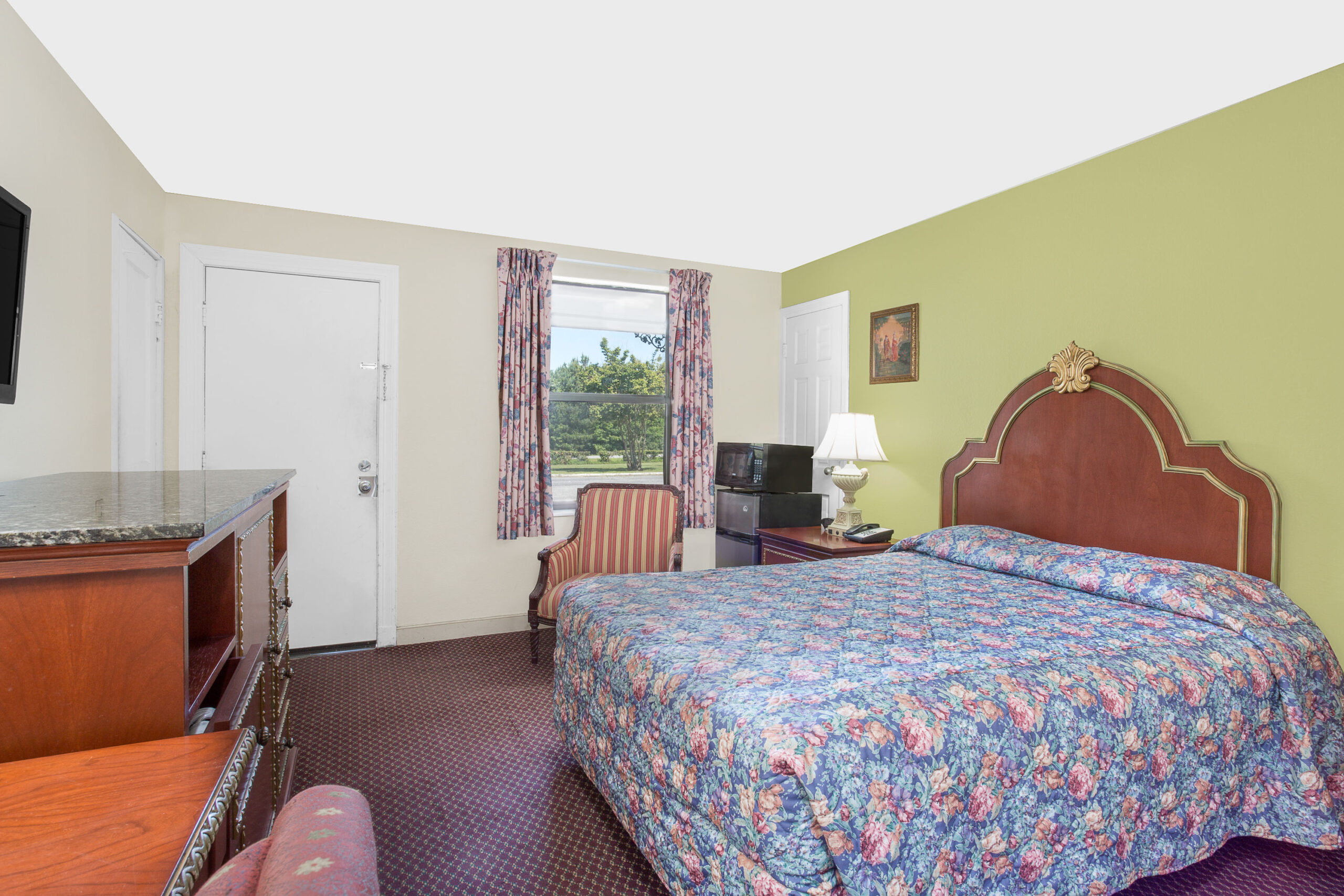 Hotel room with king bed, green accent wall, and TV.