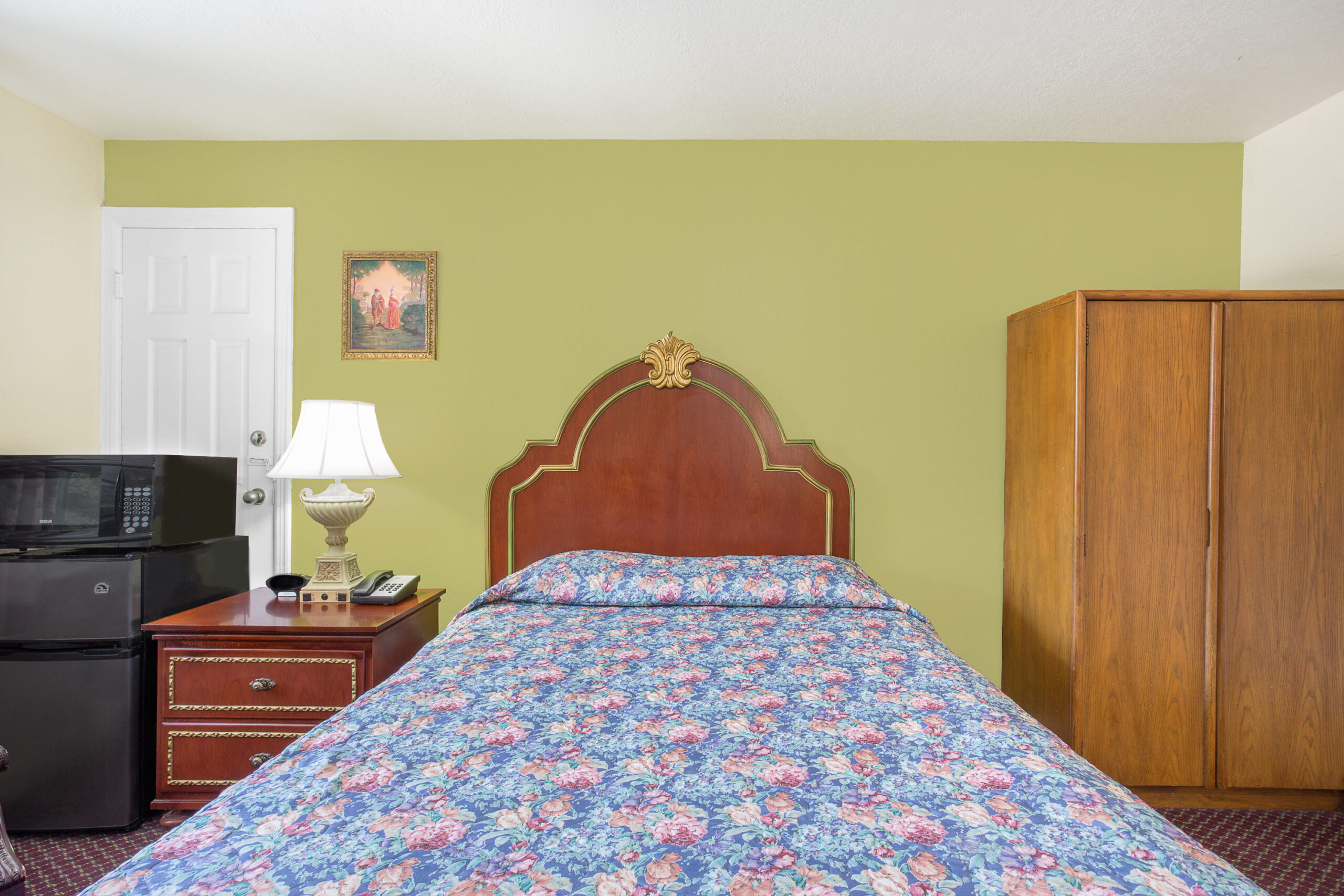 Hotel room with king bed, green wall, and wooden furniture.