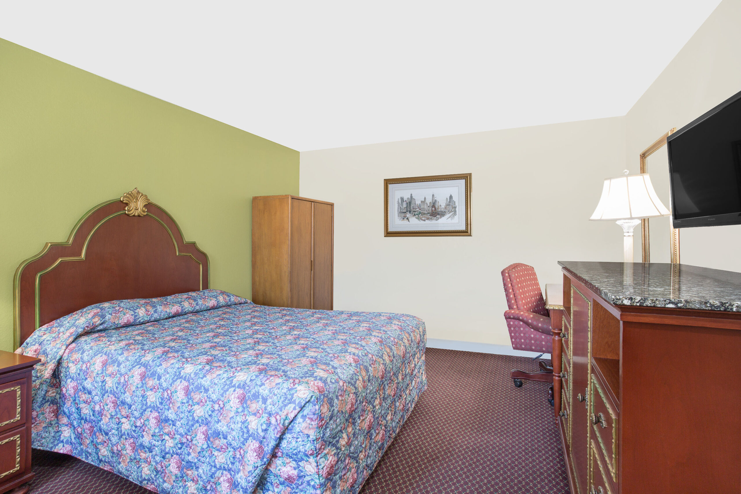 Hotel room with king bed, desk, and wall-mounted TV.