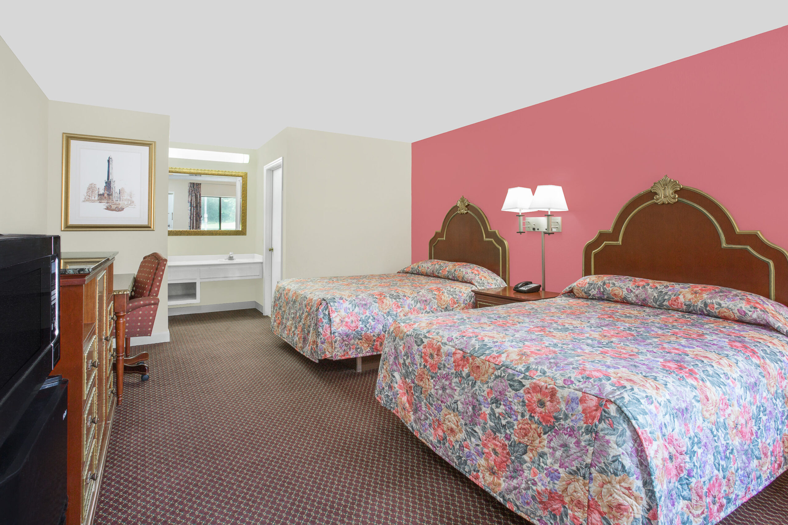 Hotel room with two beds, pink accent wall, and desk.