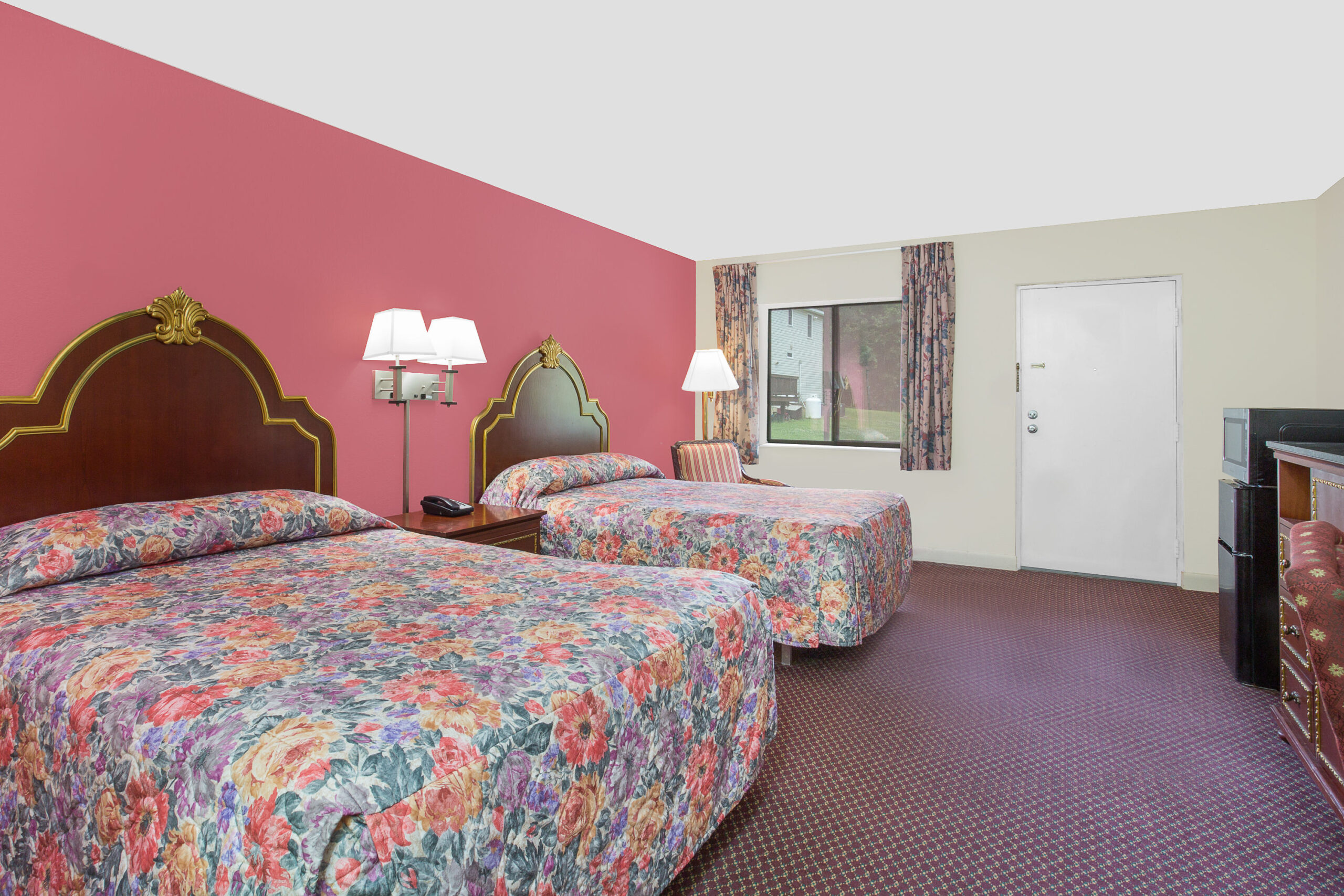 Hotel room with two beds, pink wall, and window view.