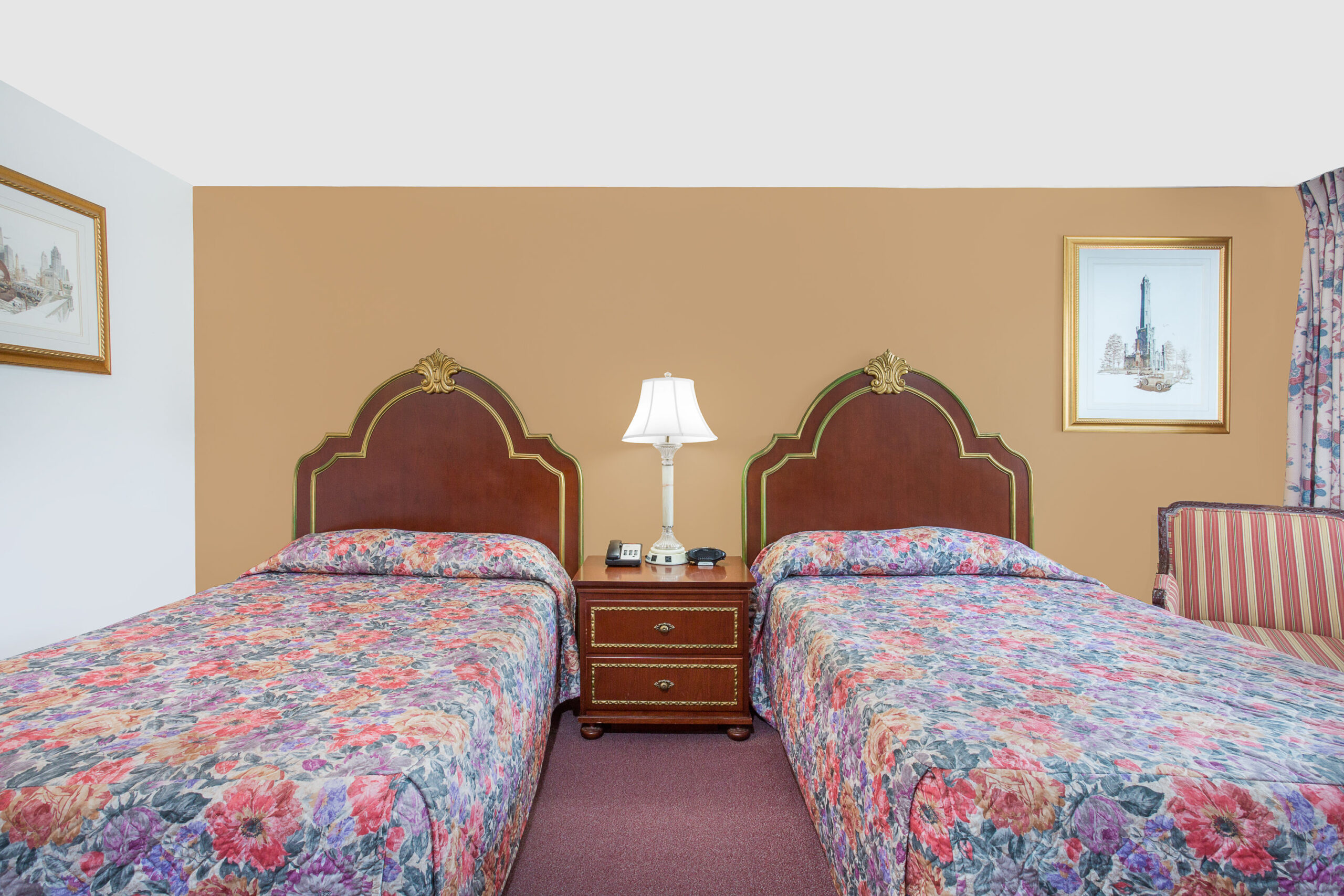 Hotel room with two beds, brown accent wall, and nightstand.