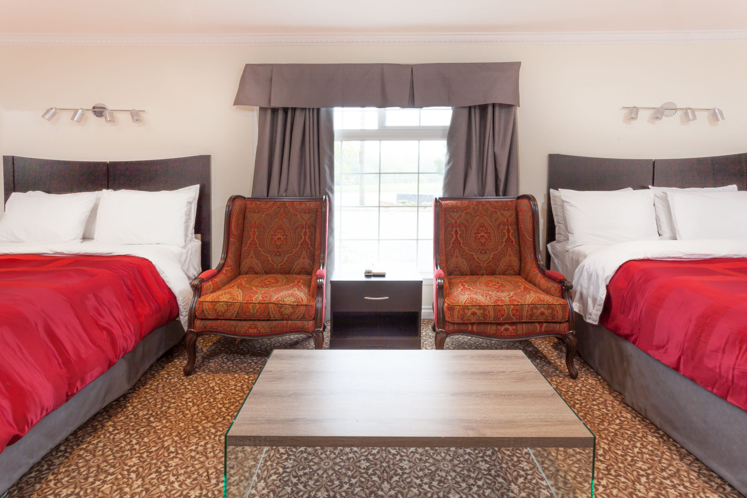 A spacious motel room with a king-sized bed, two red armchairs, a small dining table, a microwave, and a TV mounted on the wall.