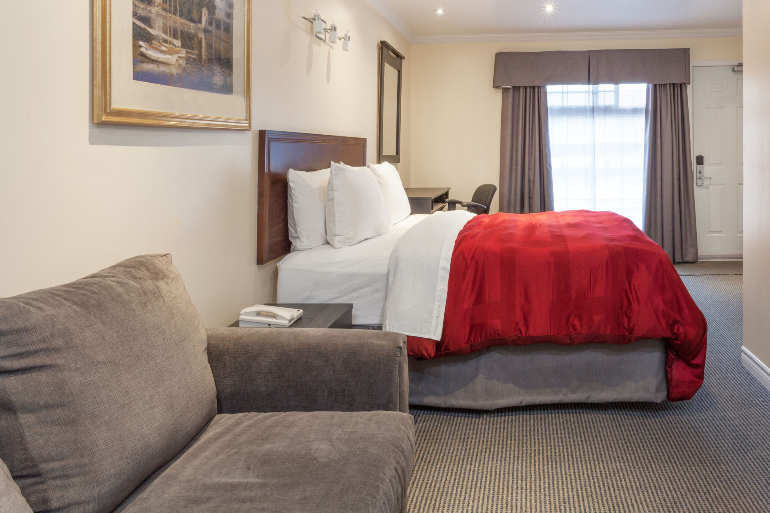 A cozy motel room with a king-sized bed, a wooden desk, a chair, and a TV on a dresser.