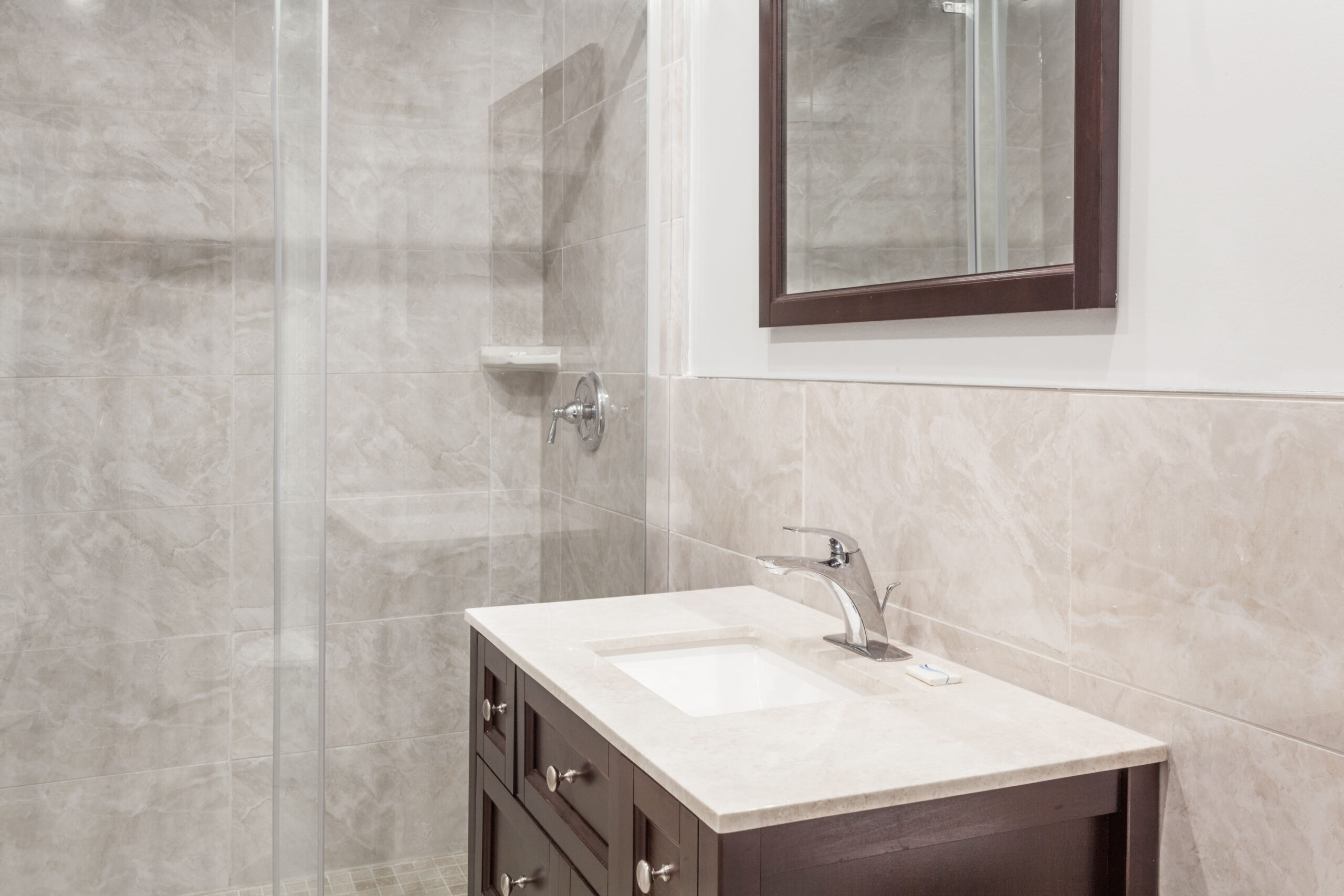 A clean and bright bathroom with a tiled shower, a bathtub, a sink with a marble countertop, and a mirror above the sink.