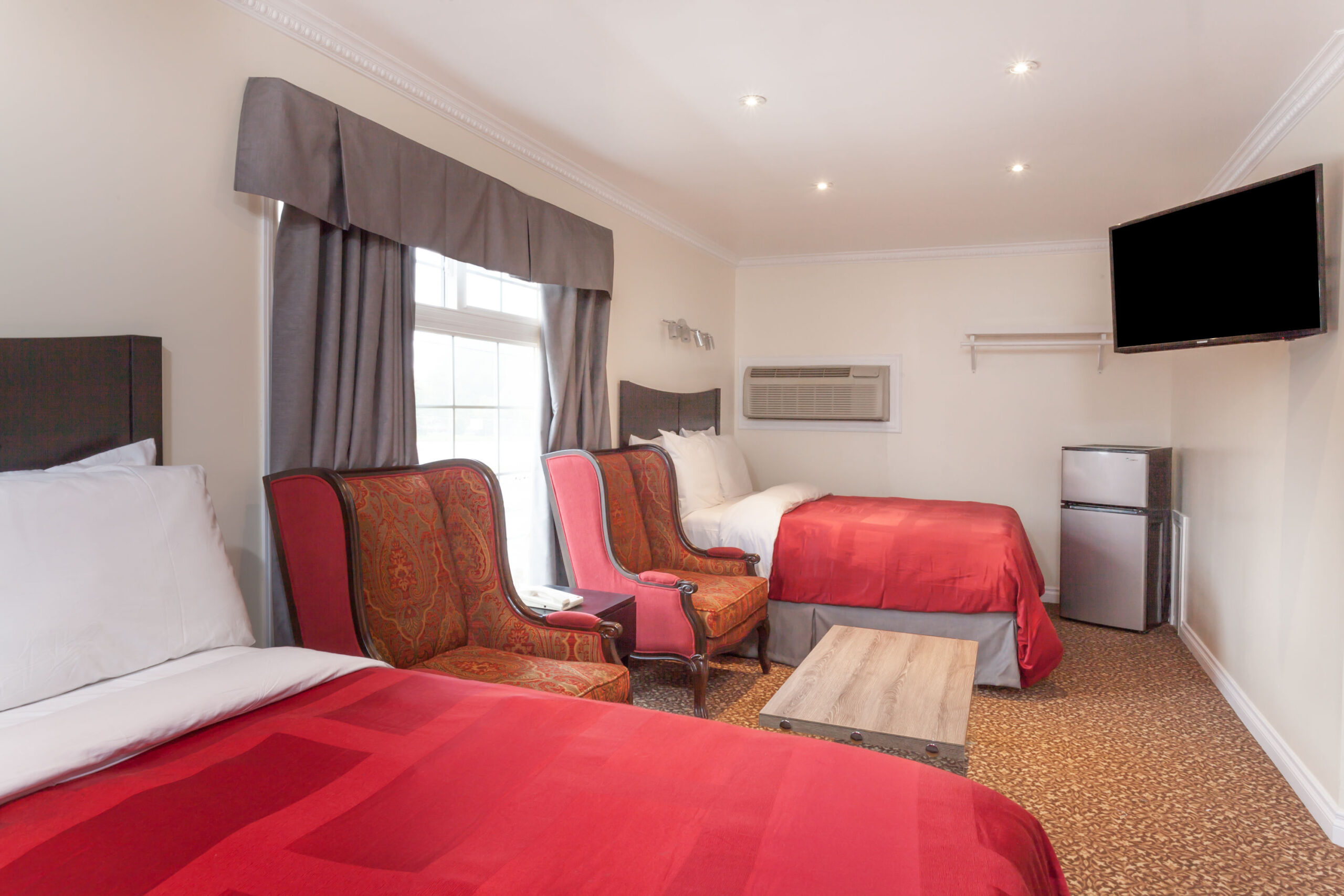 Two beds with red bedding, chairs.
