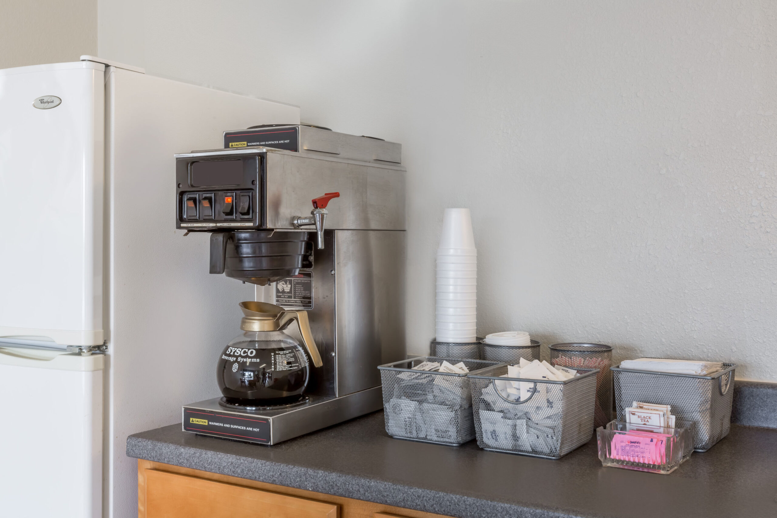 Coffee station with coffee maker and supplies on counter.