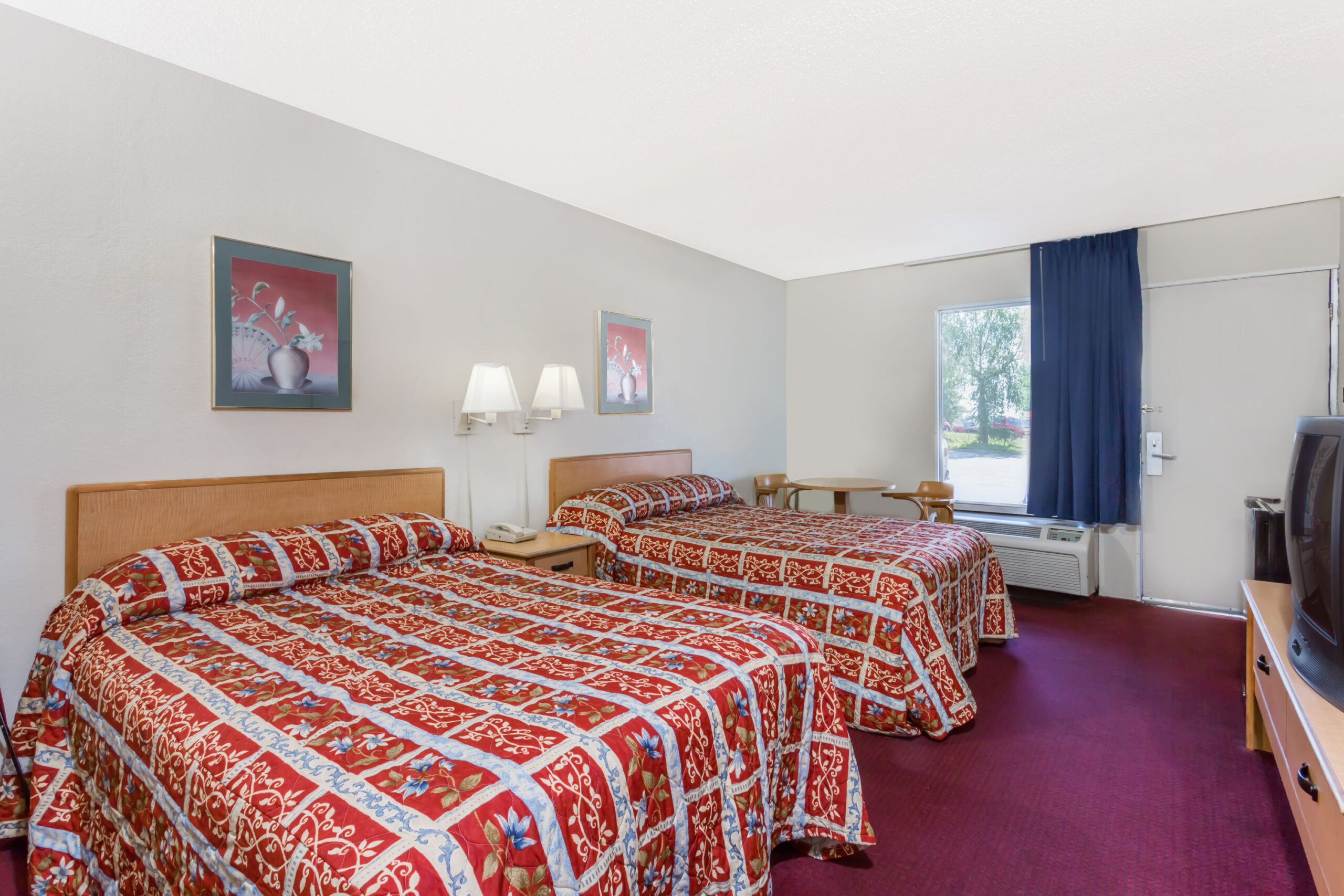 Hotel room with two double beds, TV, and window.