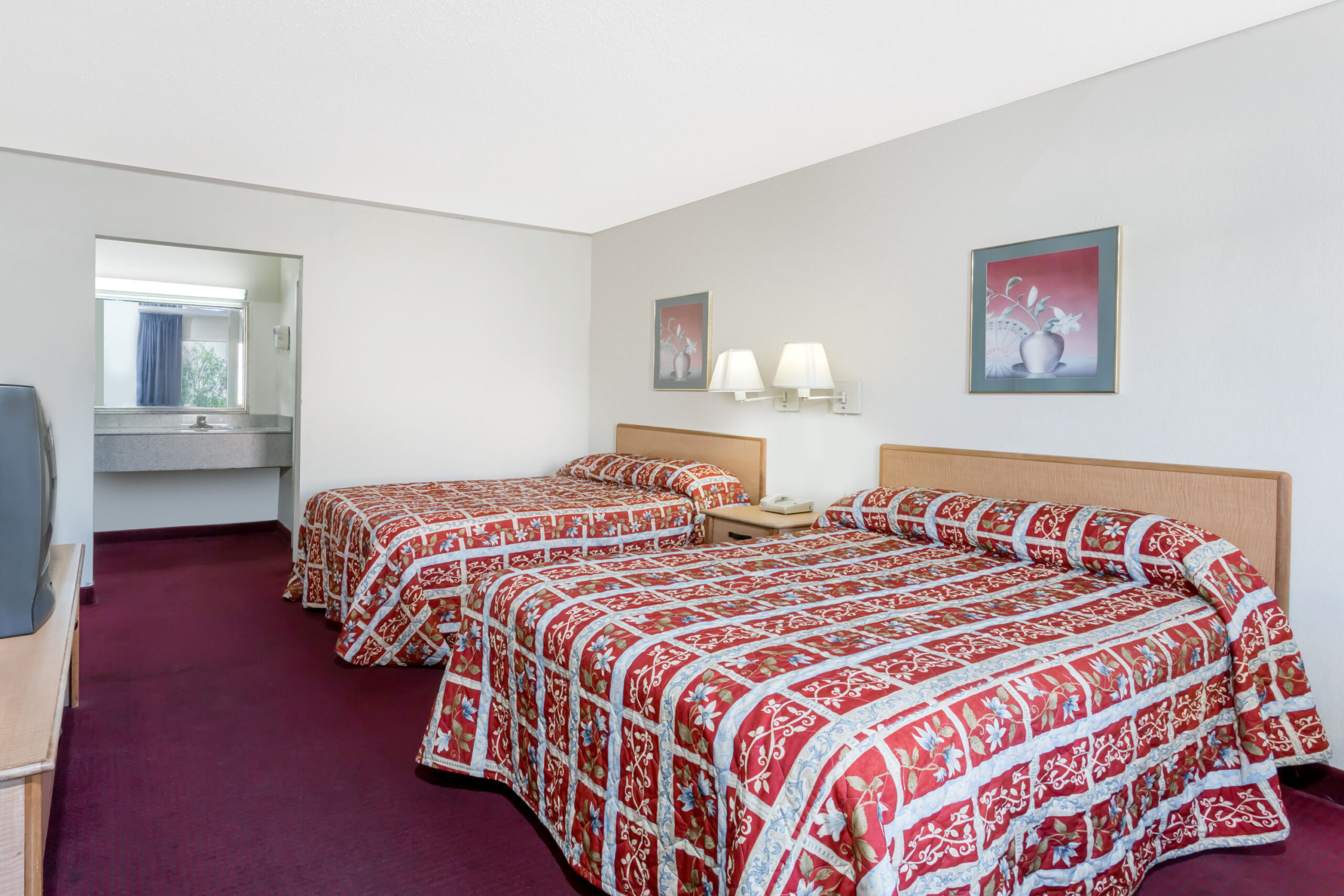 Hotel room with two double beds, TV, and burgundy carpet.