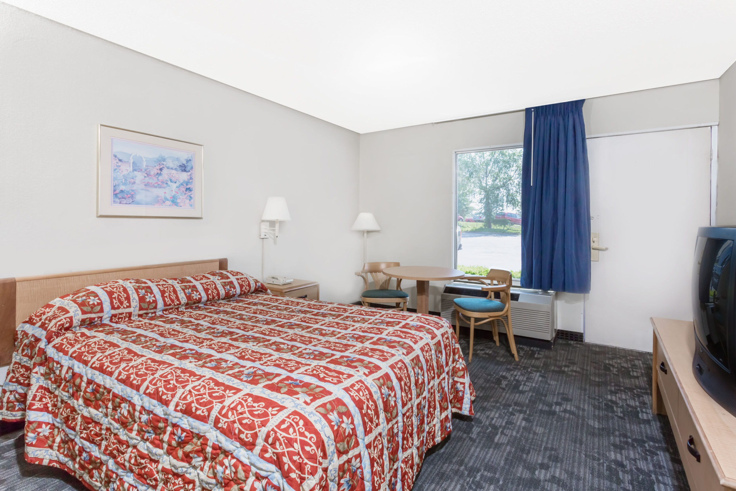 Hotel room with king bed, TV, and window with curtains.
