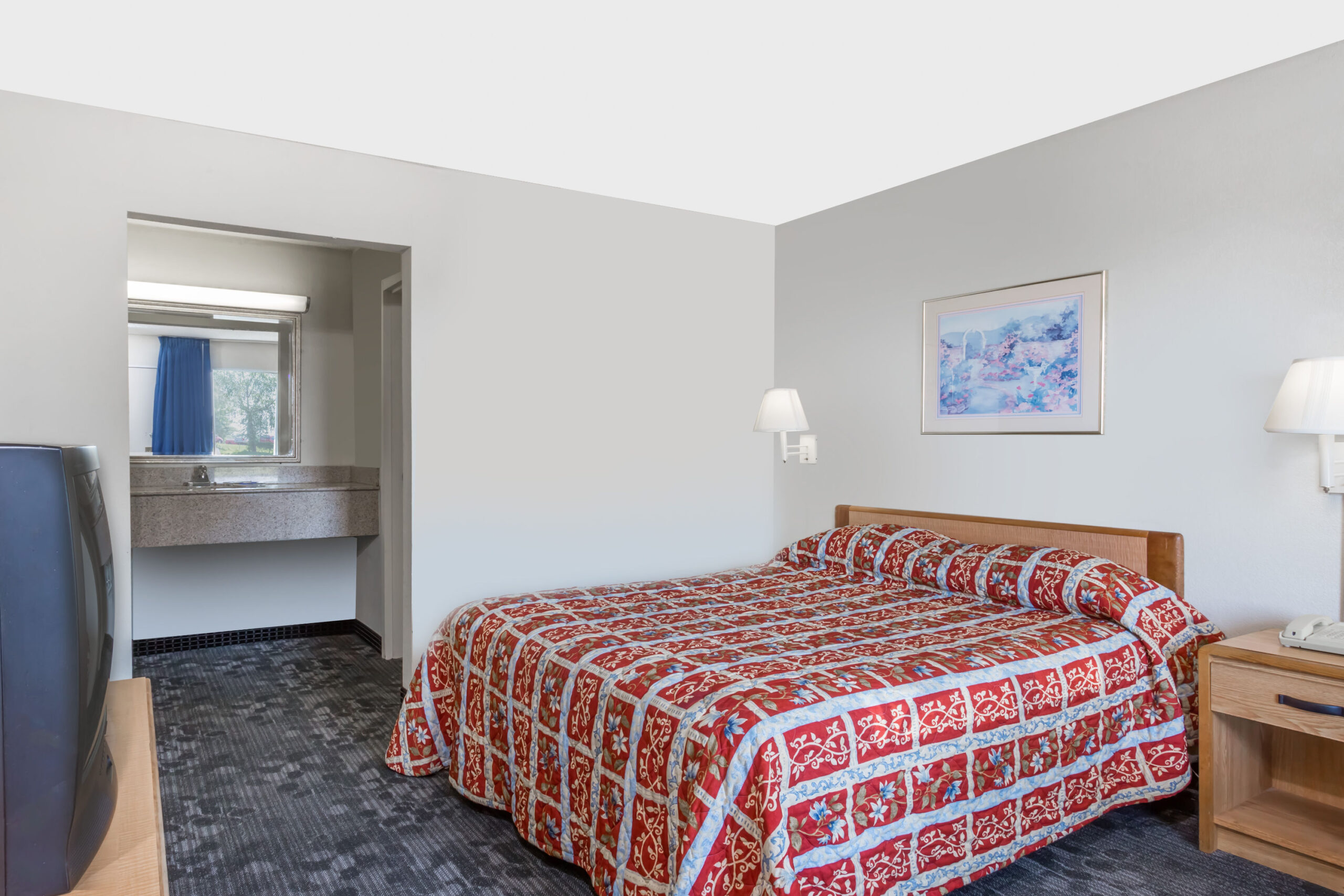 Bed with red quilt in hotel room.