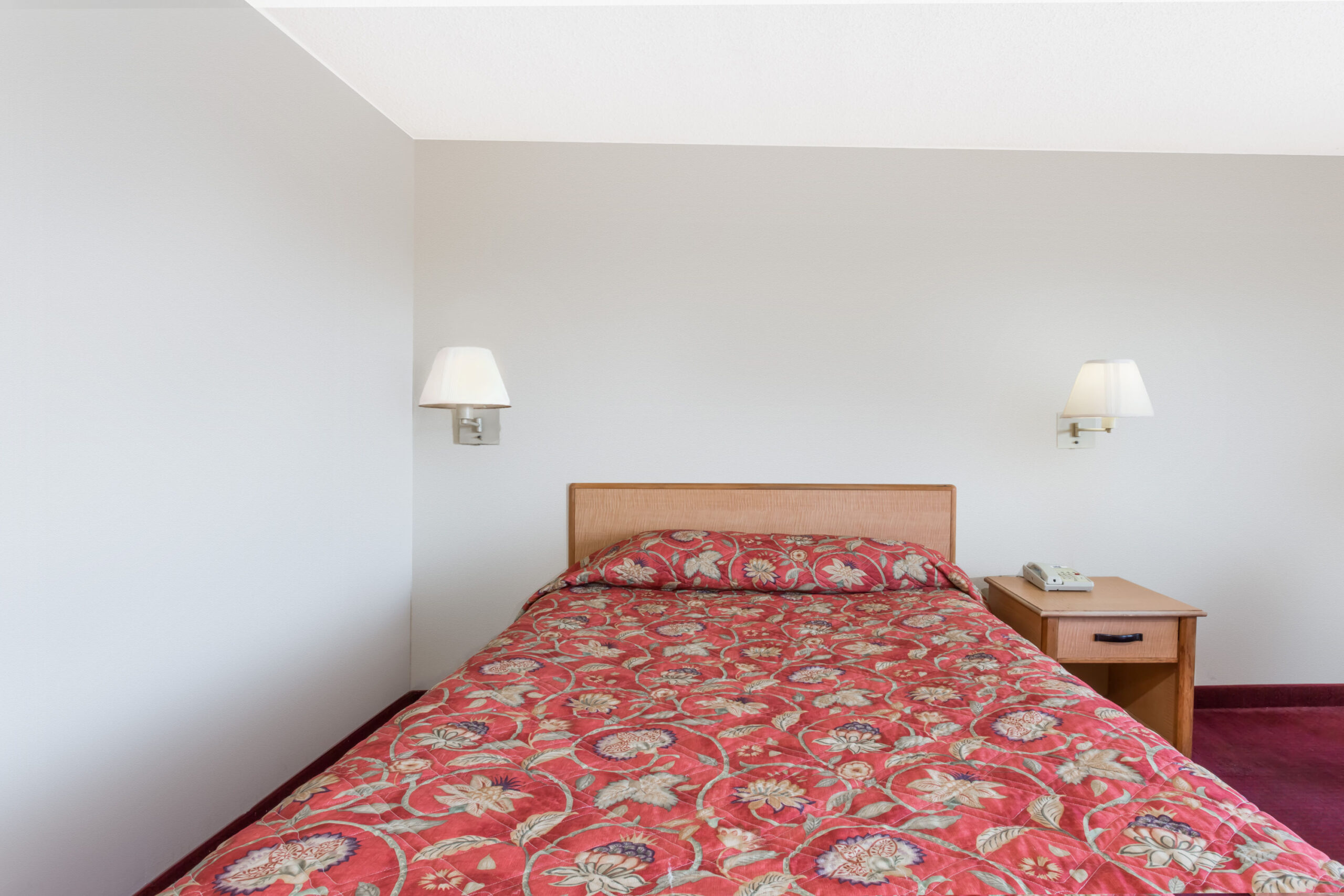 Single bed with patterned red quilt.
